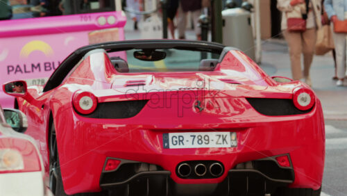 Video - Cannes, France - October 4, 2025: Rear view of a red convertible Ferrari car driving through a city street