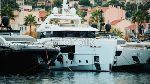 Video - Panoramic view of superyachts lined up in a marina, framed by palm trees and pastel houses on the hillside