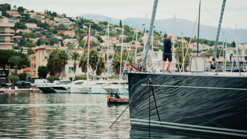 Video - Cannes, France - October 20, 2025: A man stands on the deck of a moored yacht while a small wooden boat sails past in the harbor