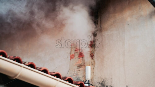 Video - A close up of dense white smoke billowing from an old brick chimney against a faded beige wall