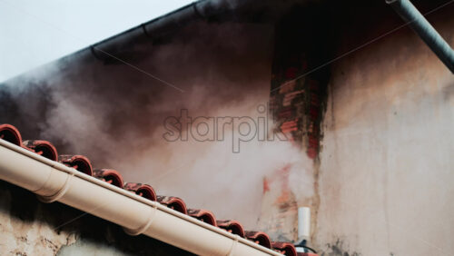 Video - A close up of dense white smoke billowing from an old brick chimney against a faded beige wall