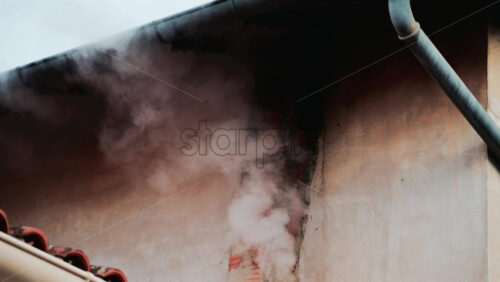 Video - A close up of dense white smoke billowing from an old brick chimney against a faded beige wall