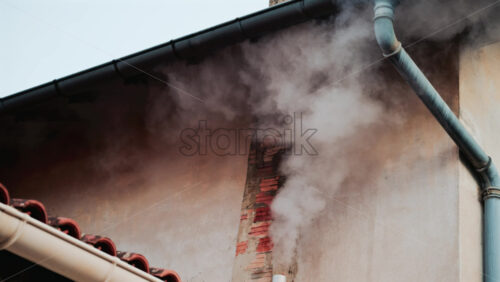 Video - A close up of dense white smoke billowing from an old brick chimney against a faded beige wall
