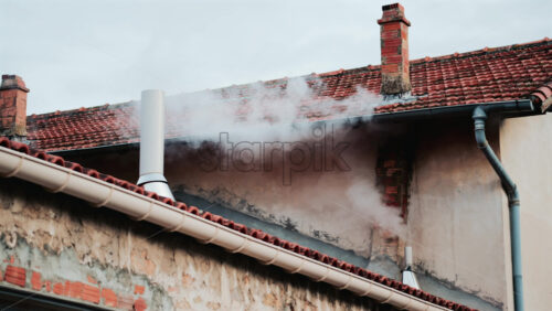 Video - A close up of dense white smoke billowing from an old brick chimney against a faded beige wall