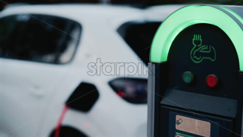 Video - Close up of a sleek black and green electric car charging station, its neon lit rim glowing in the dusk