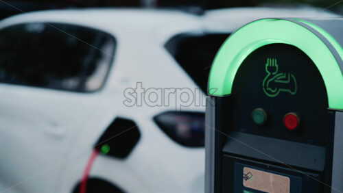 Video - Close up of a sleek black and green electric car charging station, its neon lit rim glowing in the dusk