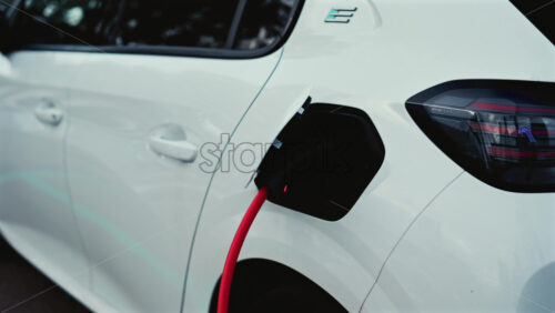 Video - Cannes, France - October 22, 2025: A white Peugeot e-208 is shown charging, the red cable plugged into its rear port