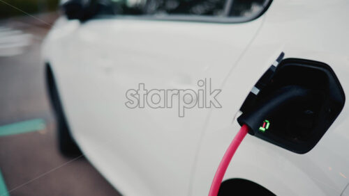 Video - A white car is shown charging, the red cable plugged into its rear port