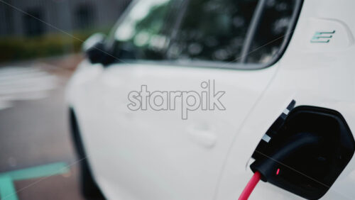 Video - A white car is shown charging, the red cable plugged into its rear port