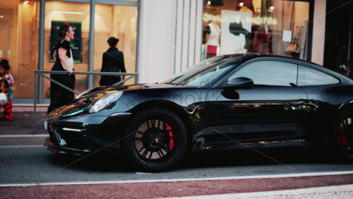 Video - Cannes, France - October 31, 2025: A glossy black Porsche 911 gleams under soft evening light, its curves perfectly defined