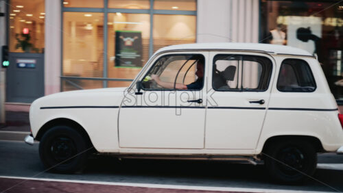 Video - Cannes, France - October 31, 2025: A cream colored Renault 4 glides down a city street, headlights glowing softly as it passes shopfronts and pedestrians