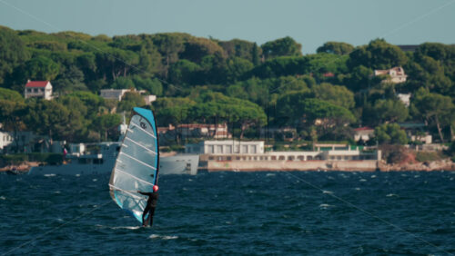 Video - Cannes, France - October 4, 2025: Two windsurfers gliding across blue sea with lush green coastline and luxury villas in the background