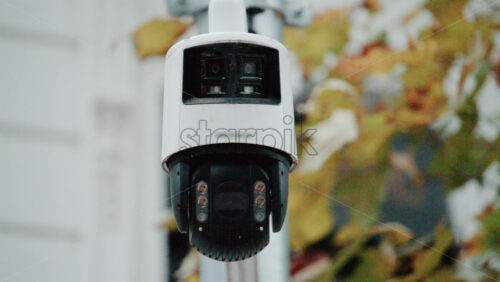 Video - Close up of a security surveillance camera mounted on a pole with blurred autumn leaves in the background