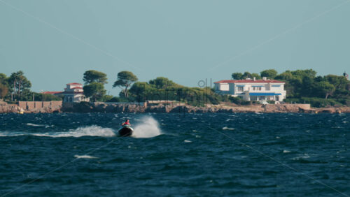 Video - Cannes, France - October 4, 2025: Black speed boat creating splashes while racing on deep blue sea near rocky coastline and luxury villas