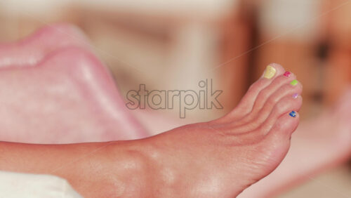 Video - Close up of a woman's foot with colorful toenail polish relaxing at the beach under sunlight