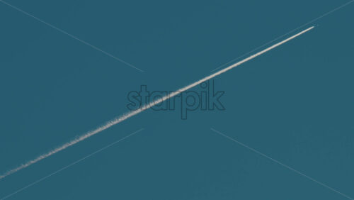 Video - Airplane flying high above leaving long contrails in a clear blue sky