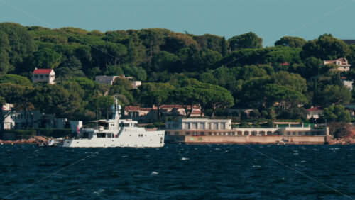 Video - Luxury white yacht sailing near Mediterranean coastline with elegant villas surrounded by trees