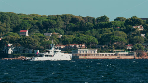 Video - Luxury white yacht sailing near Mediterranean coastline with elegant villas surrounded by trees