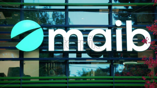 Video - Chisinau, Moldova - October 1, 2025: Modern glass building facade with the illuminated maib logo and red autumn leaves in the foreground