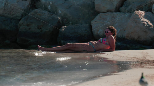 Video - Cannes, France - October 5, 2025: Woman in colorful bikini sunbathing on the beach by the rocks