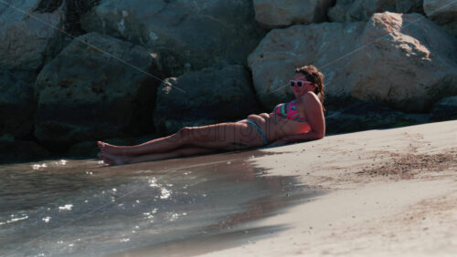 Video - Cannes, France - October 5, 2025: Woman in colorful bikini sunbathing on the beach by the rocks
