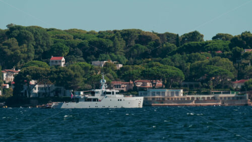 Video - Luxury white yacht sailing near Mediterranean coastline with elegant villas surrounded by trees