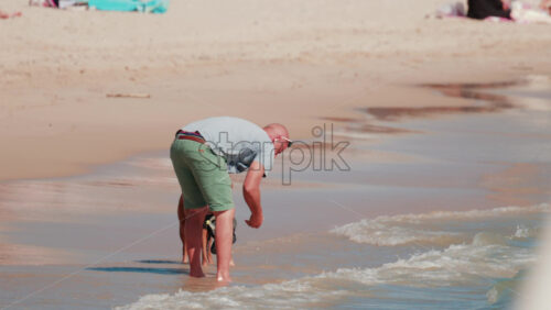 Video - Cannes, France - October 5, 2025: Man bending down to play with his dog in shallow sea water on a sandy beach
