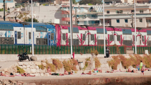 Video - Cannes, France - October 5, 2025: Blue train passing along the French Riviera coastline with beachgoers in the foreground
