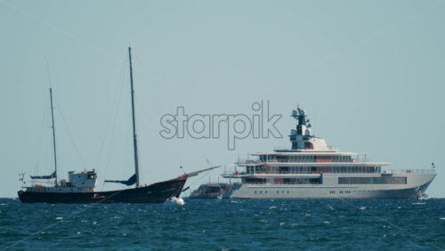 Video - Contrast between an old sailboat and a modern luxury yacht floating on calm Mediterranean waters