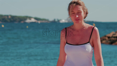 Video - Woman in a white swimsuit walking in shallow sea water on a sunny day in Cannes, France