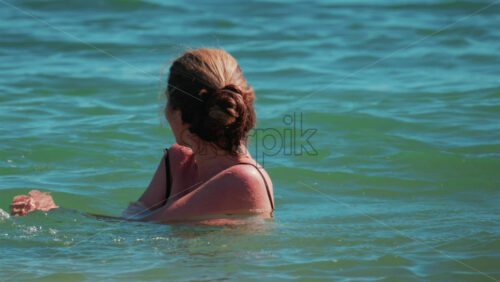 Video - Woman floating in turquoise sea water, enjoying the sunlight and peaceful surroundings