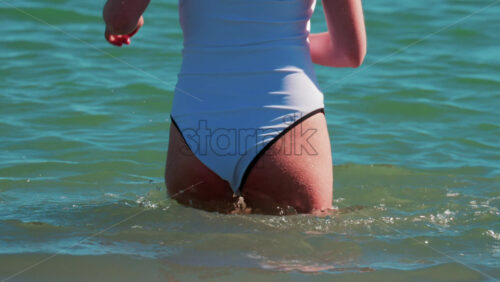 Video - A young woman walks slowly into the calm turquoise water on a sunny summer day in Cannes, France