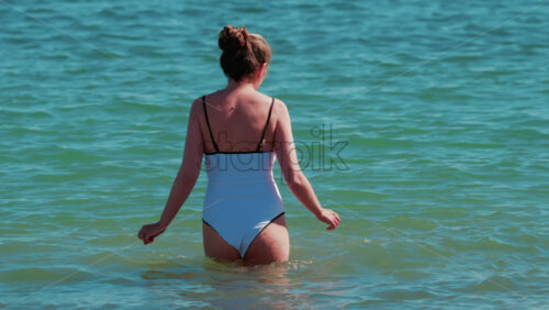 Video - A young woman walks slowly into the calm turquoise water on a sunny summer day in Cannes, France