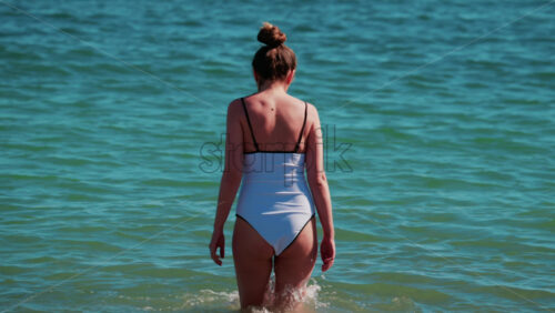 Video - A young woman walks slowly into the calm turquoise water on a sunny summer day in Cannes, France