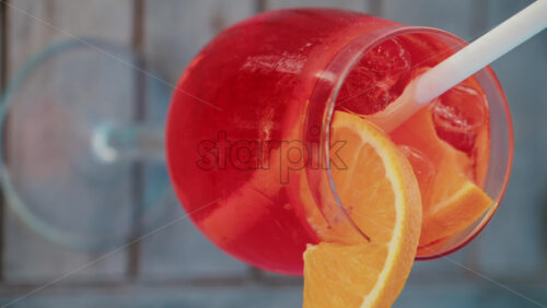 Video - Close up of a refreshing red orange cocktail with orange slice and ice cubes, captured outdoors on a sunny day in Cannes. Vertical