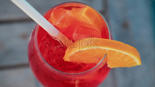 Video - Close up of a refreshing red orange cocktail with orange slice and ice cubes, captured outdoors on a sunny day in Cannes