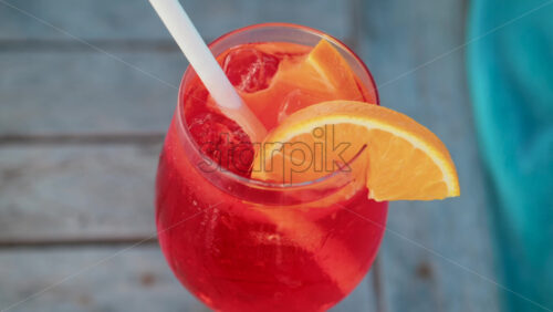 Video - Close up of a refreshing red orange cocktail with orange slice and ice cubes, captured outdoors on a sunny day in Cannes