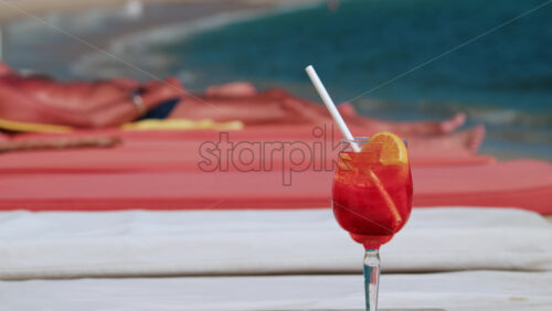Video - Close up of a refreshing red orange cocktail with orange slice and ice cubes, captured outdoors on a sunny day in Cannes