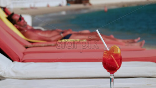 Video - Close up of a refreshing red orange cocktail with orange slice and ice cubes, captured outdoors on a sunny day in Cannes