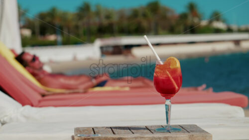 Video - Close up of a refreshing red orange cocktail with orange slice and ice cubes, captured outdoors on a sunny day in Cannes