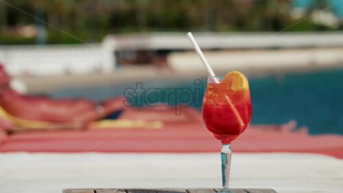 Video - Close up of a refreshing red orange cocktail with orange slice and ice cubes, captured outdoors on a sunny day in Cannes