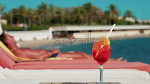 Video - Close up of a refreshing red orange cocktail with orange slice and ice cubes, captured outdoors on a sunny day in Cannes
