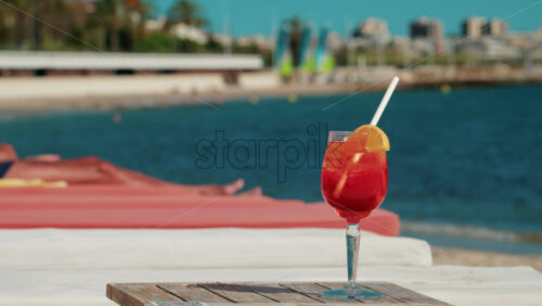 Video - Close up of a refreshing red orange cocktail with orange slice and ice cubes, captured outdoors on a sunny day in Cannes