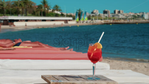 Video - Close up of a refreshing red orange cocktail with orange slice and ice cubes, captured outdoors on a sunny day in Cannes