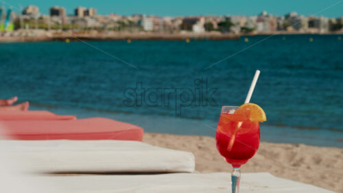 Video - Refreshing red orange cocktail with ice and orange slice against the deep blue Mediterranean Sea