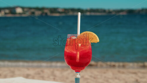 Video - Refreshing red orange cocktail with ice and orange slice against the deep blue Mediterranean Sea