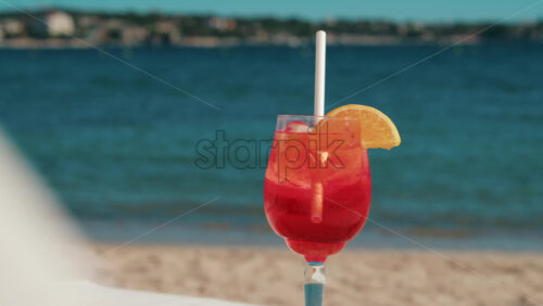 Video - Refreshing red orange cocktail with ice and orange slice against the deep blue Mediterranean Sea