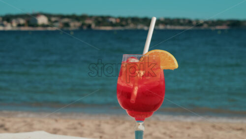 Video - Refreshing red orange cocktail with ice and orange slice against the deep blue Mediterranean Sea