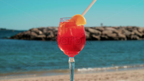 Video - Refreshing red orange cocktail with ice and orange slice against the deep blue Mediterranean Sea