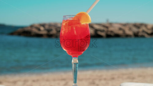 Video - Refreshing red orange cocktail with ice and orange slice against the deep blue Mediterranean Sea